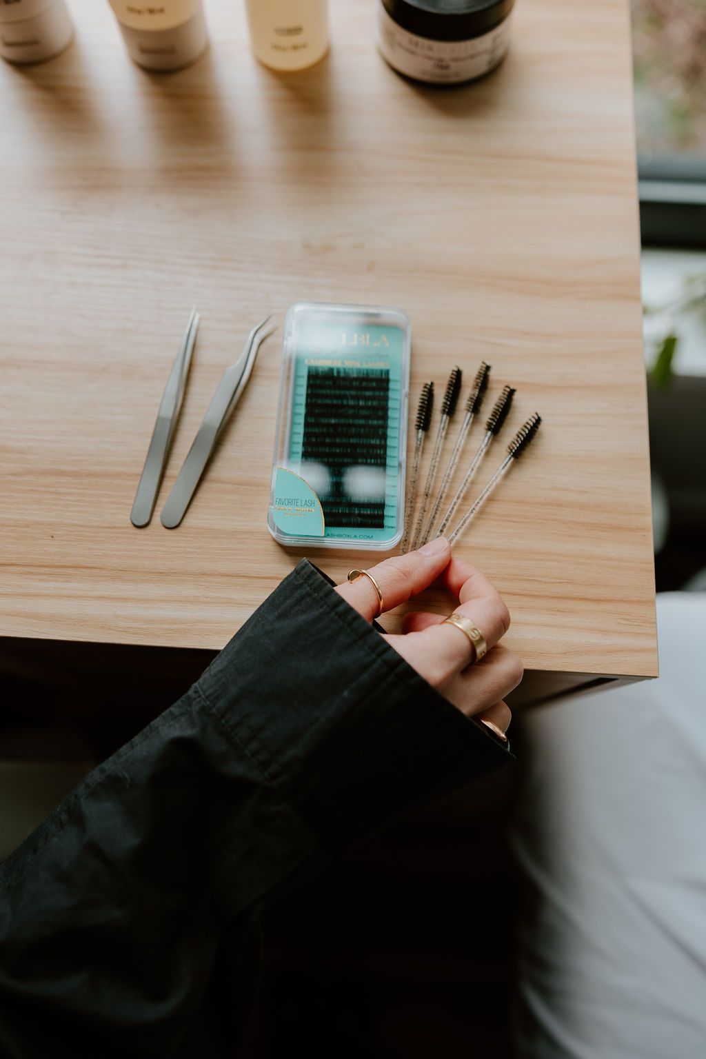 Tweezers, a lash tray and lash wands laid out on a wooden table
