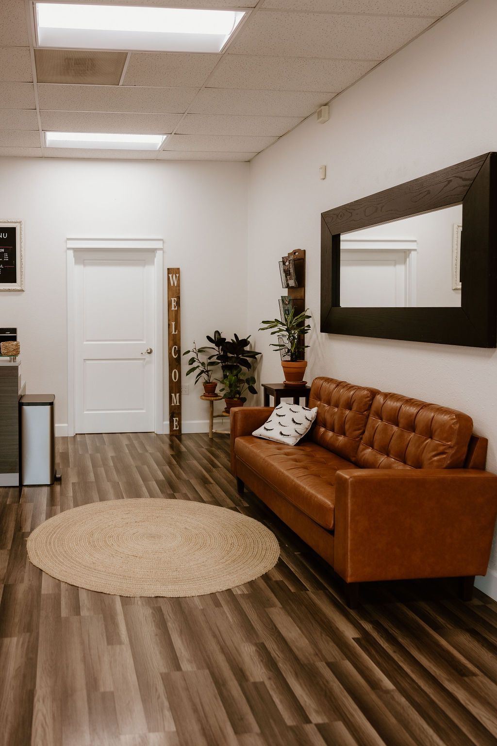 Salon lounge with a tan leather sofa, round rug and framed mirror