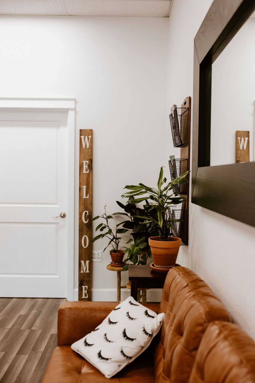 Salon entrance with a welcome sign, plants and a lash-print pillow on the sofa